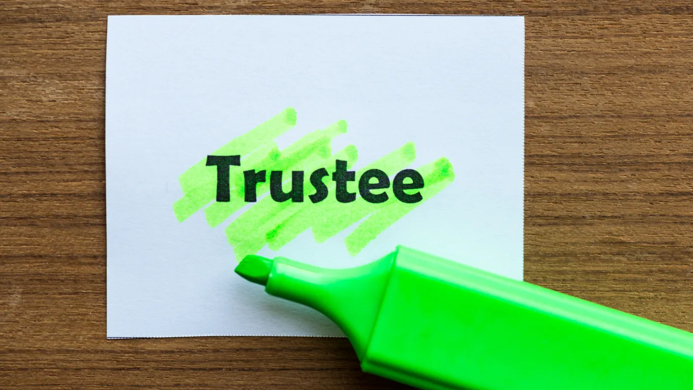 A piece of white paper on a wooden desk with the word &lsquo;Trustee&rsquo; highlighted in green, alongside a green highlighter