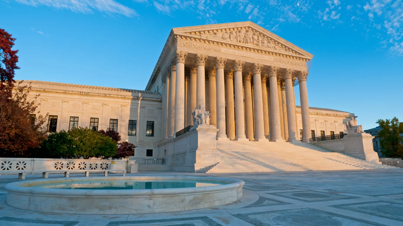 The U.S. Supreme Court building in Washington, D.C., with its columned facade lit by warm afternoon sunlight and a marble fountain in the foreground