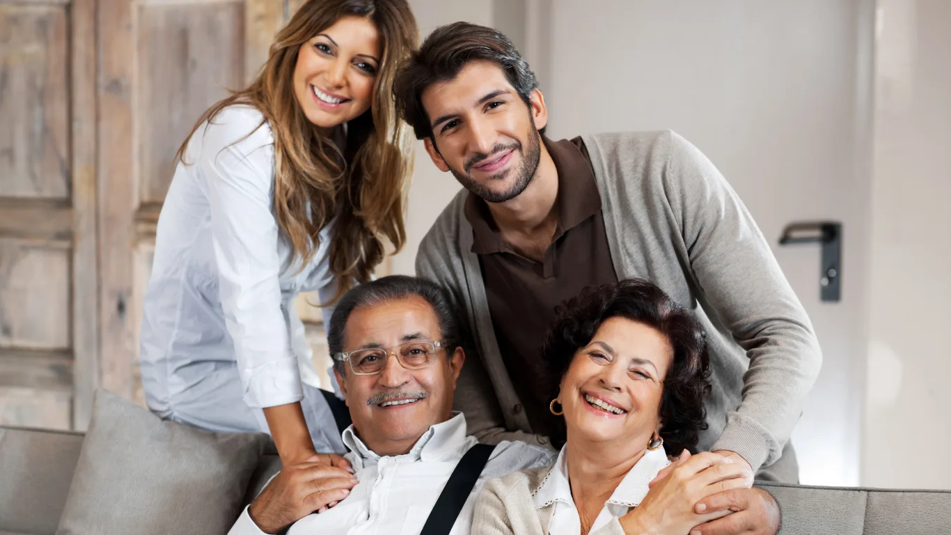 A multigenerational family, adult son and daughter with their parents, smiling together on a couch