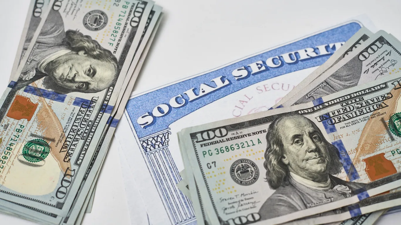 A Social Security card partially covered by stacks of hundred-dollar bills