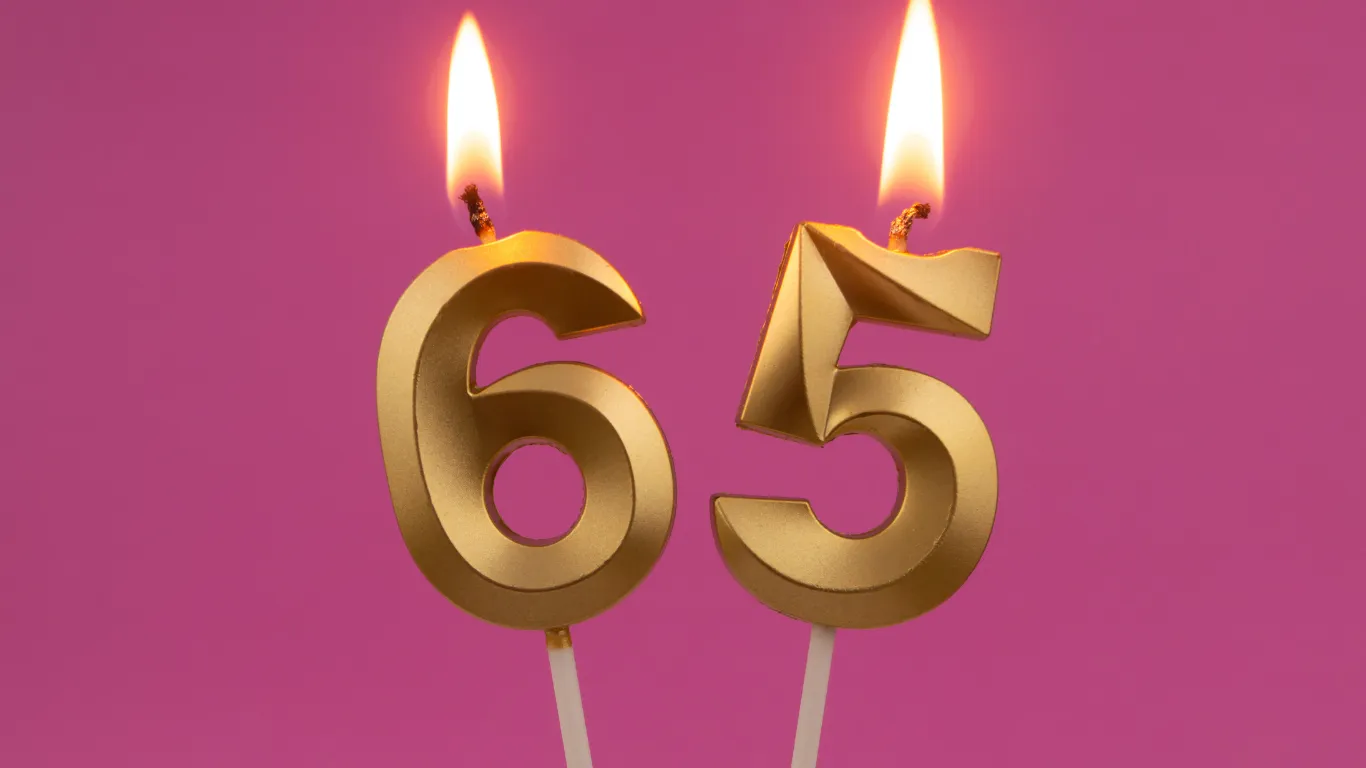Two lit gold candles shaped like the number 65 against a pink background