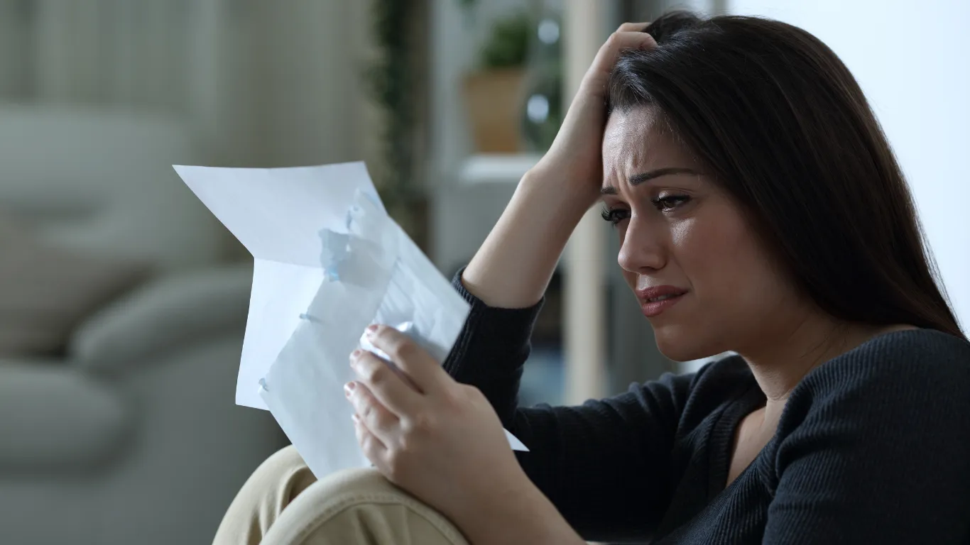 A woman looking distressed while reading an official letter and envelope from Medicaid